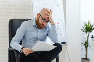 Bald man with glasses sitting in office looking worried at document.